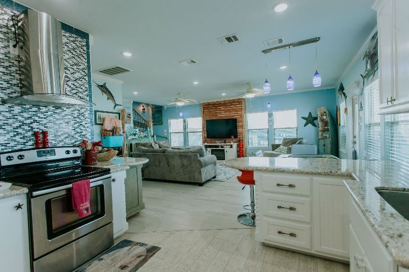 A kitchen with a stove , sink , cabinets and a living room.