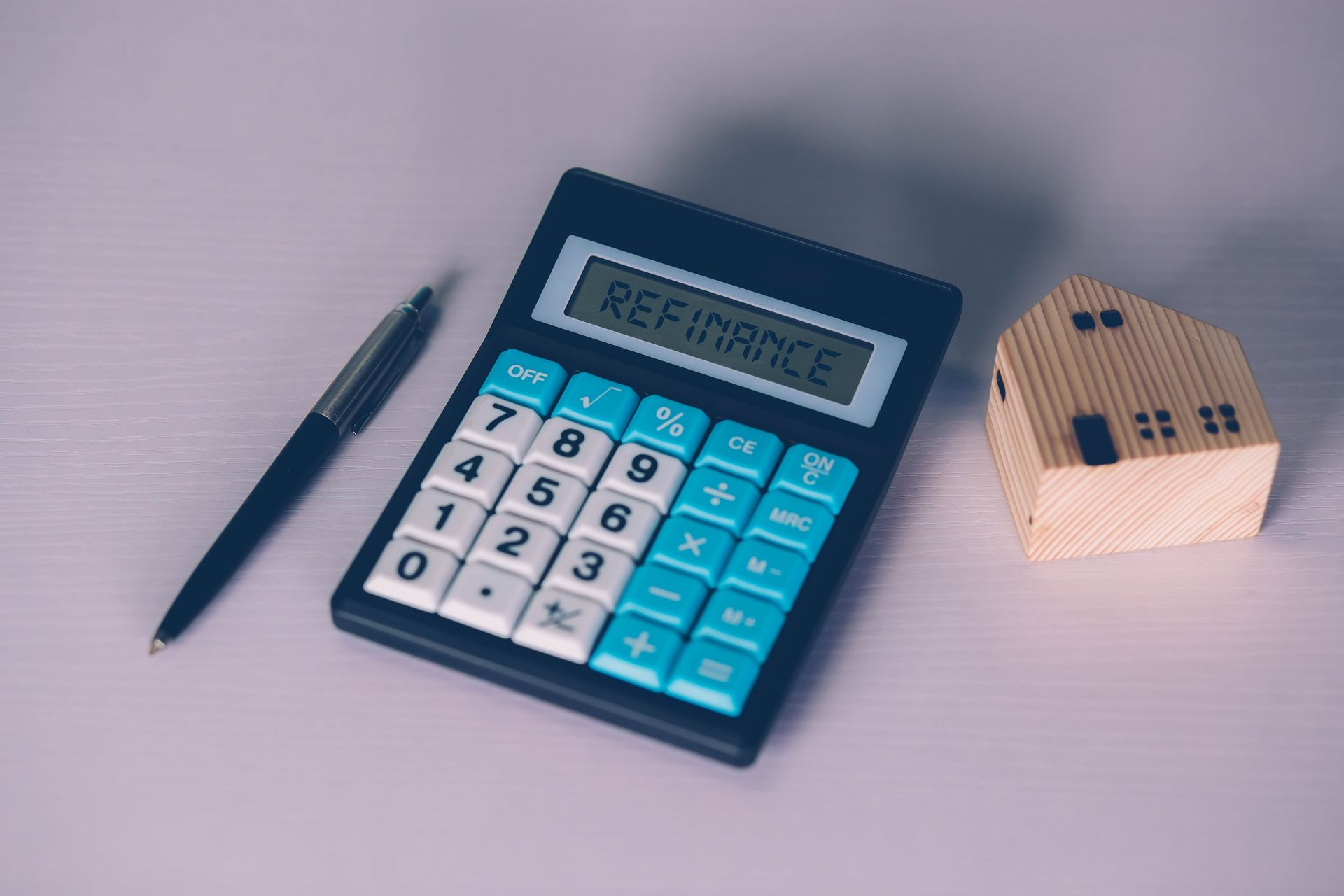 A calculator , pen and a model house on a table.