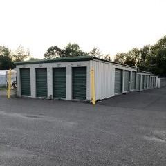 A row of storage units with green doors are lined up in a field.