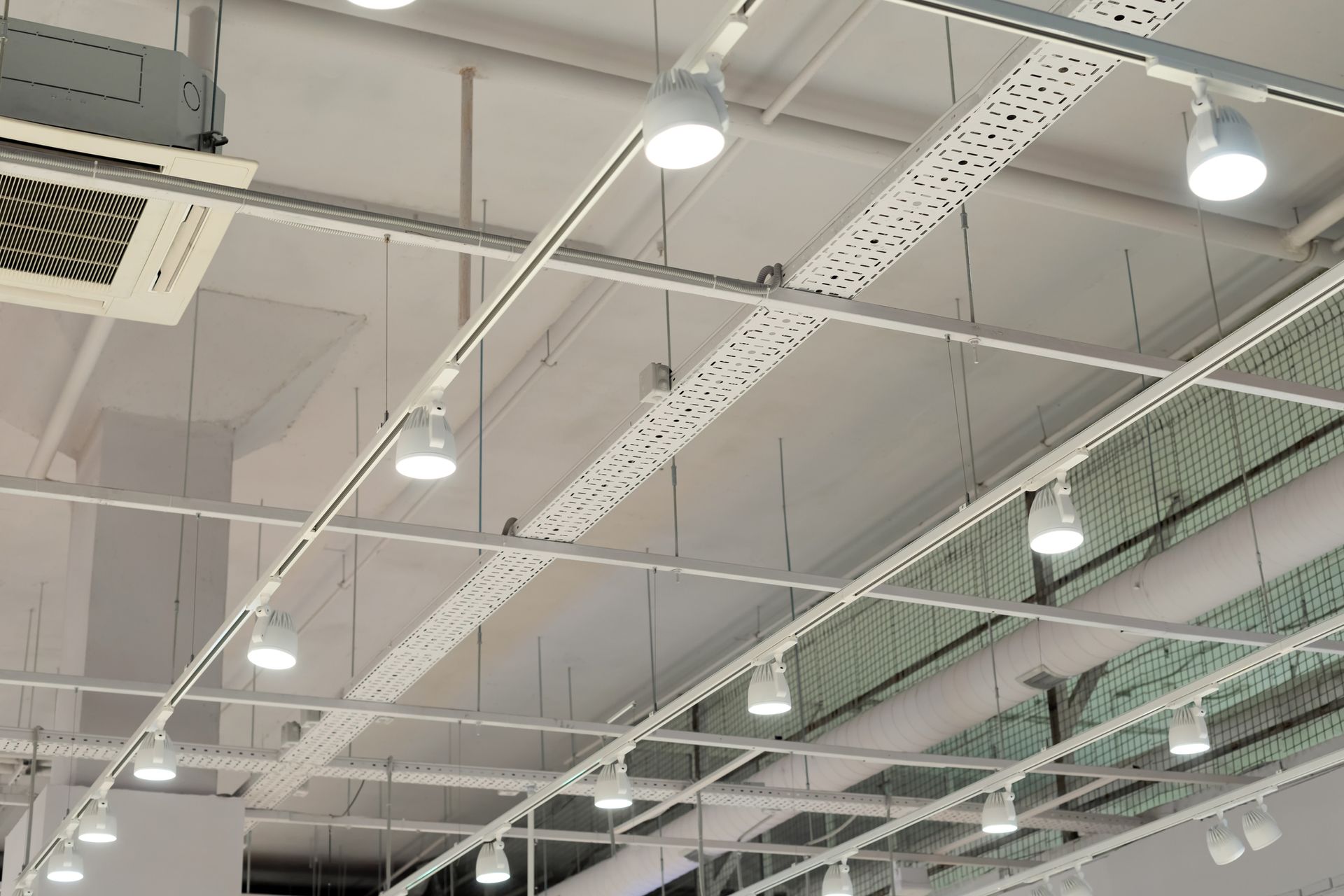 Bright white industrial lighting on the ceiling with track-mounted LED spotlights and HVAC ductwork.