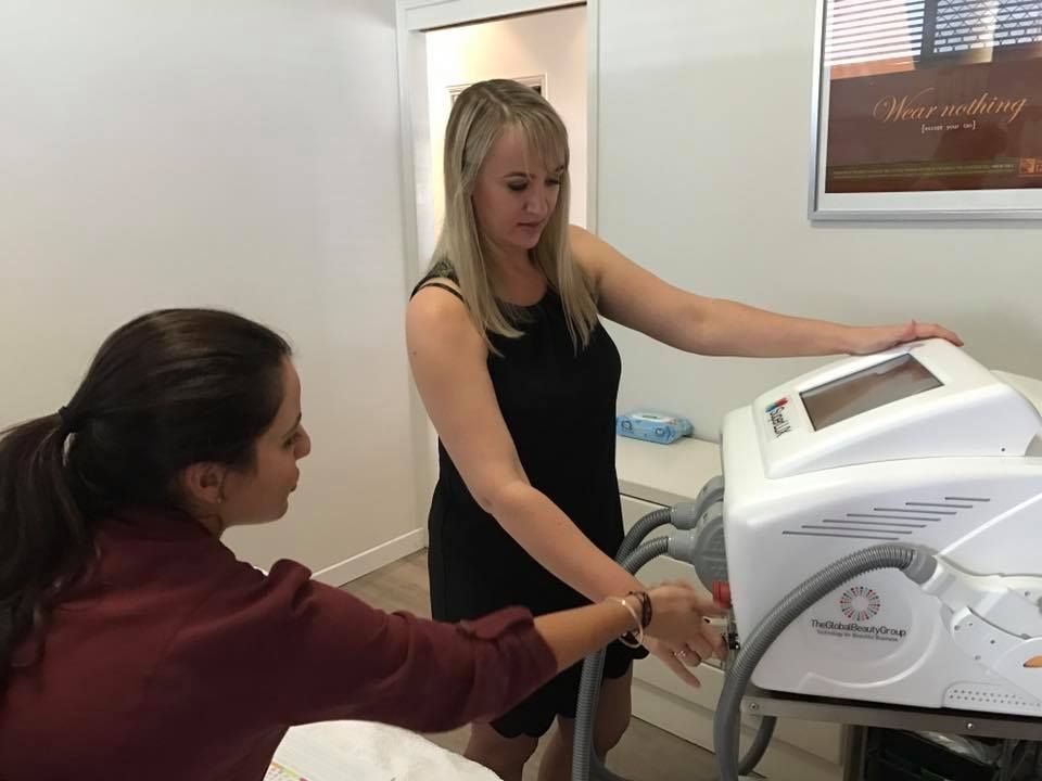Two Women Are Looking at a Machine in a Room — Erikka's All Occasion Beauty In Rockhampton City, QLD