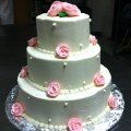 A three tiered wedding cake with pink roses and pearls on top.