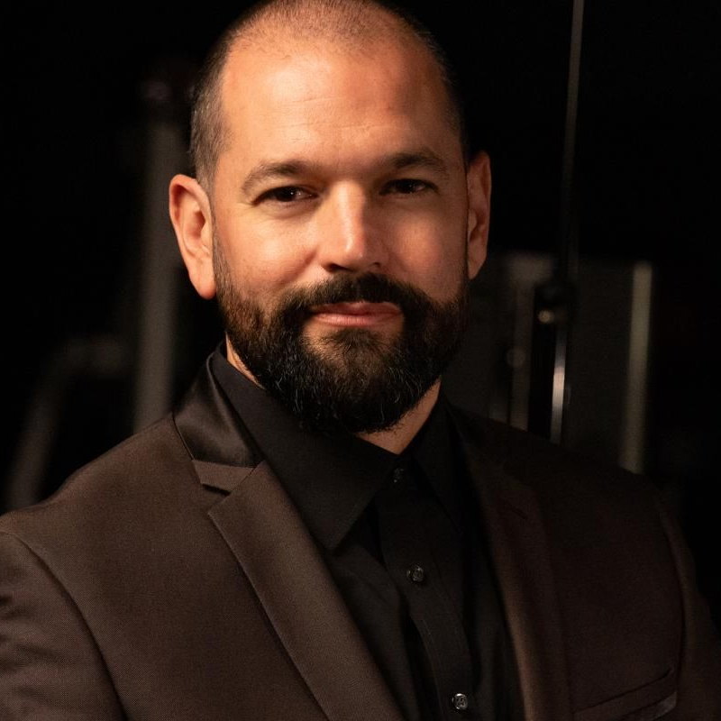 A woman in a black jacket is making a heart shape with her hands.