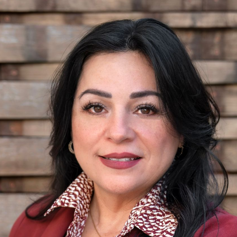A man in a blue shirt is sitting in a chair with his hand on his chin.