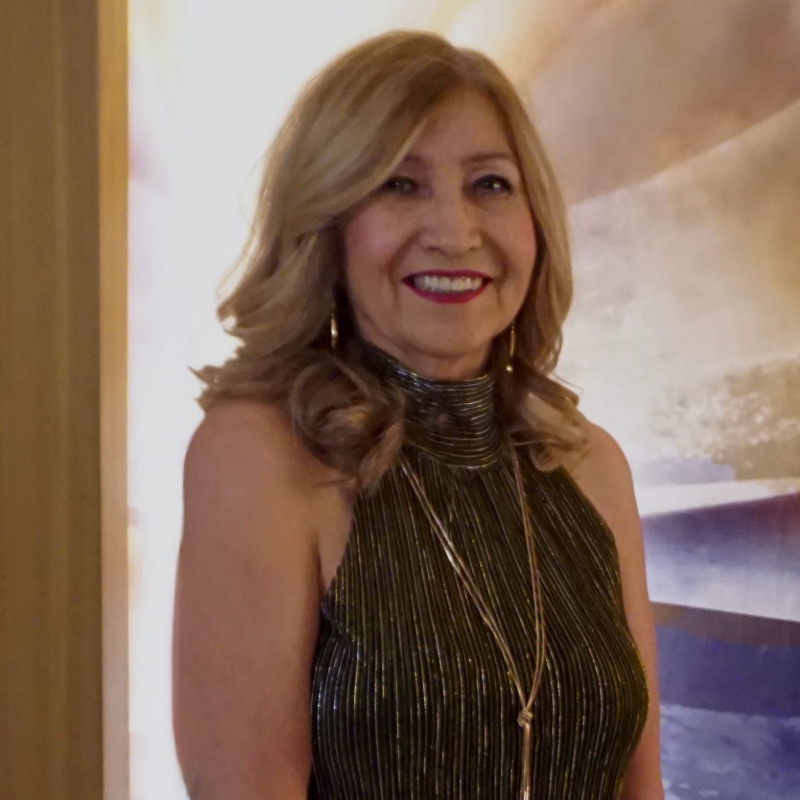 A woman in a pink off the shoulder dress is standing on a sidewalk.