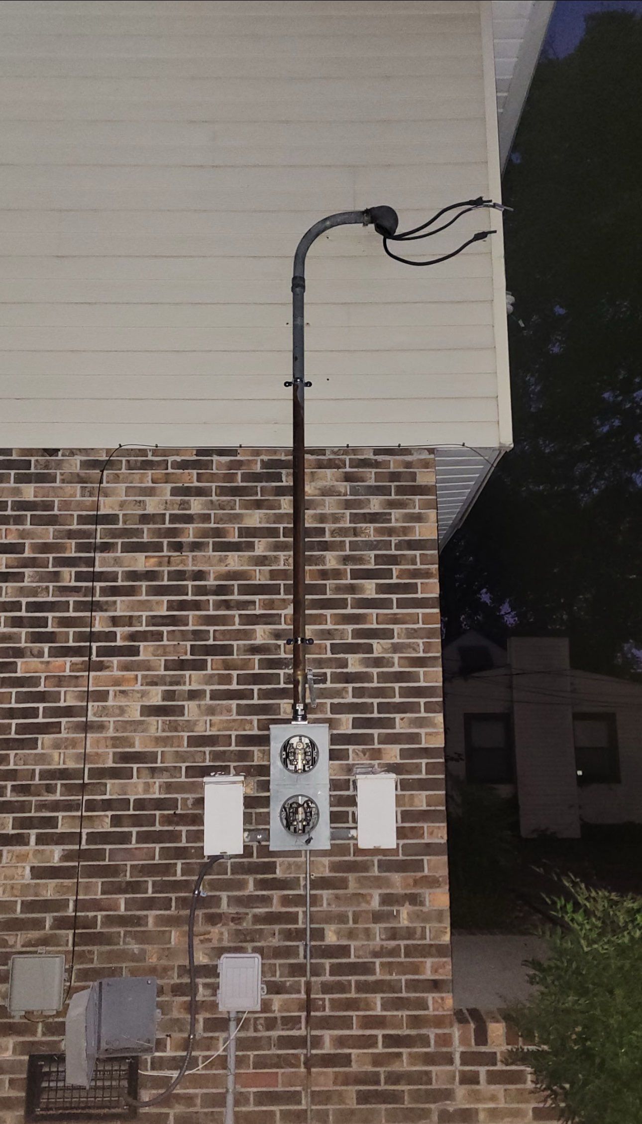 Electrical equipment mounted on brick wall, including conduits, junction boxes, and meters.