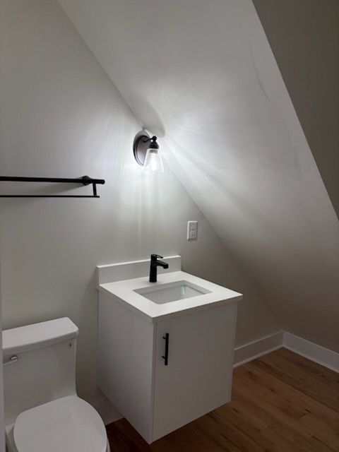 Small bathroom with white vanity, toilet, black fixtures, and sloped ceiling.