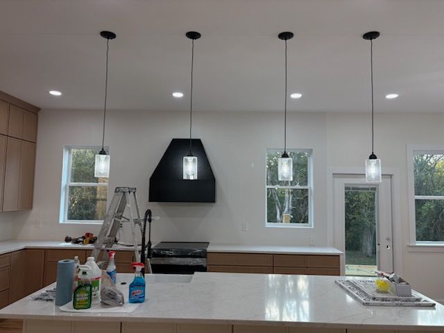 Modern kitchen with island, range, and four pendant lights. Light wood cabinets and white countertops.