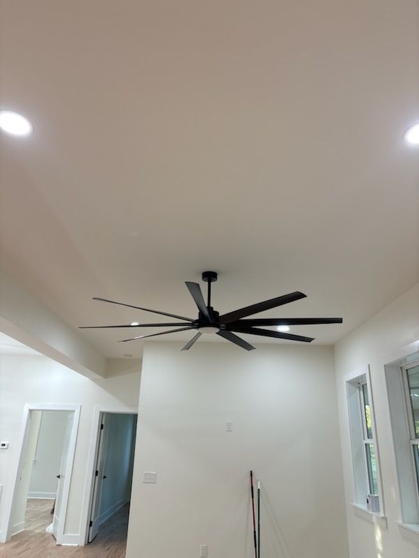 Large black ceiling fan with multiple blades, mounted on a white ceiling.