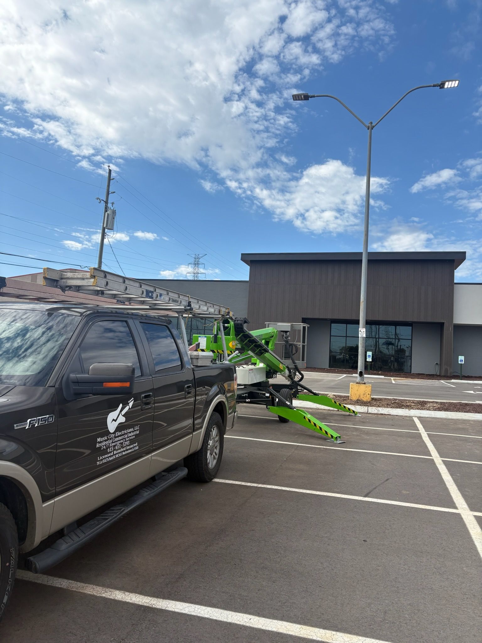 Tow truck and attached boom in parking lot in front of building on a partly cloudy day.