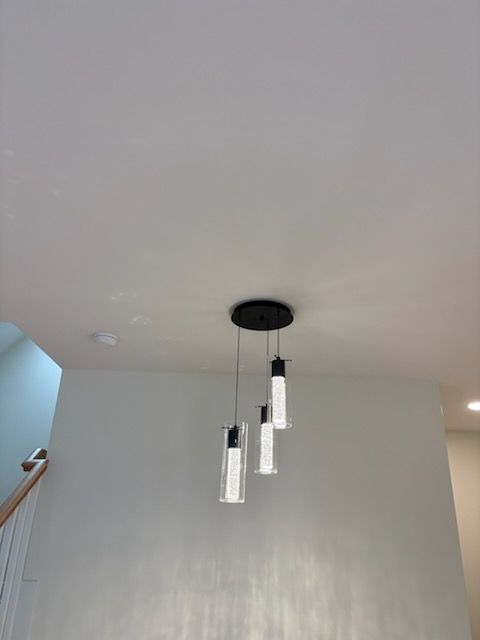 Three modern pendant lights hanging from a black ceiling fixture in a white room.
