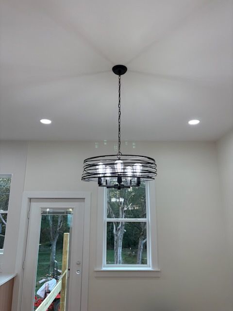Black and silver chandelier hanging from a white ceiling, recessed lights, door and window visible.