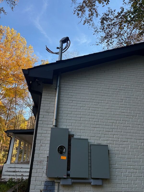 Exterior electrical panel and conduit mounted on a brick house with a satellite dish on the roof.