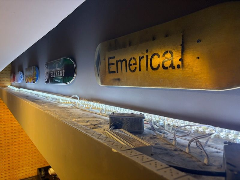 Skateboard decks with logos displayed above a strip of LED lights on a white surface.