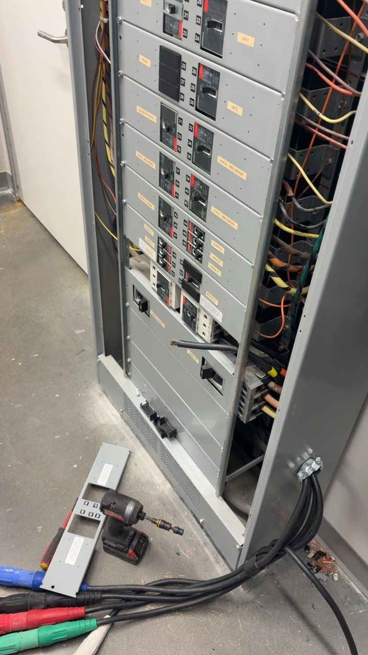 Electrical panel with exposed wiring, open panel door, and power tools on the floor.
