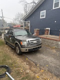 Dark pickup truck parked in front of a dark blue house. Snow falling.