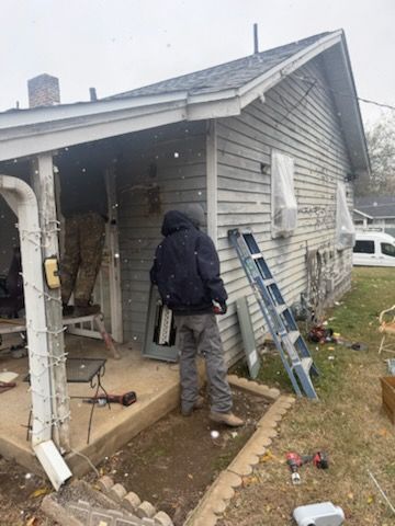 Person near house, standing in front of a ladder, working on the side of a building under cloudy skies.
