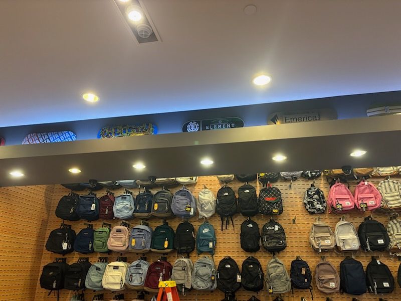 Backpacks displayed on a store wall, various colors, lit from above, retail setting.