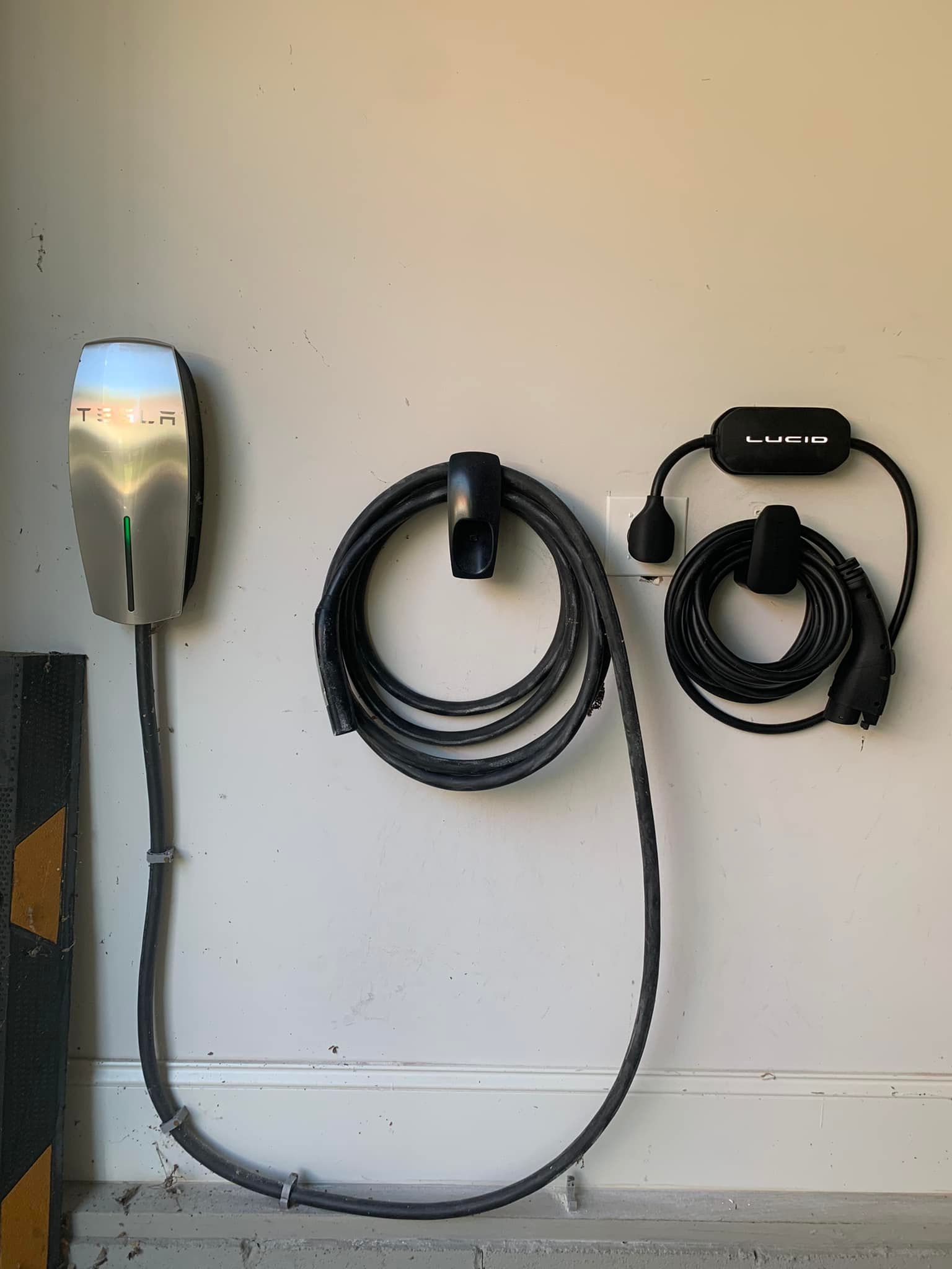 A tesla charging station is hanging on a wall next to a hose.