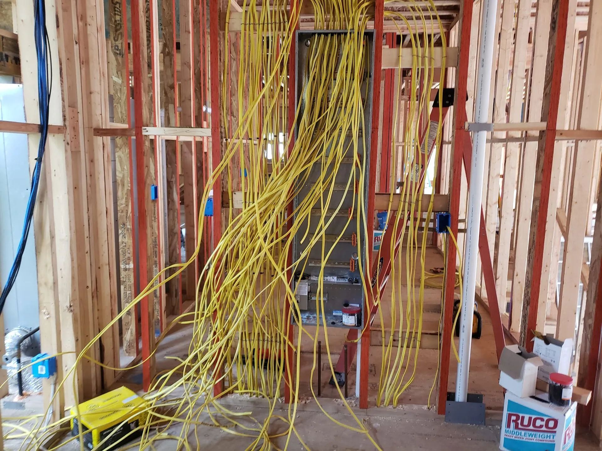 Electrical wiring in a wooden wall, cords spilling from an unfinished electrical panel.