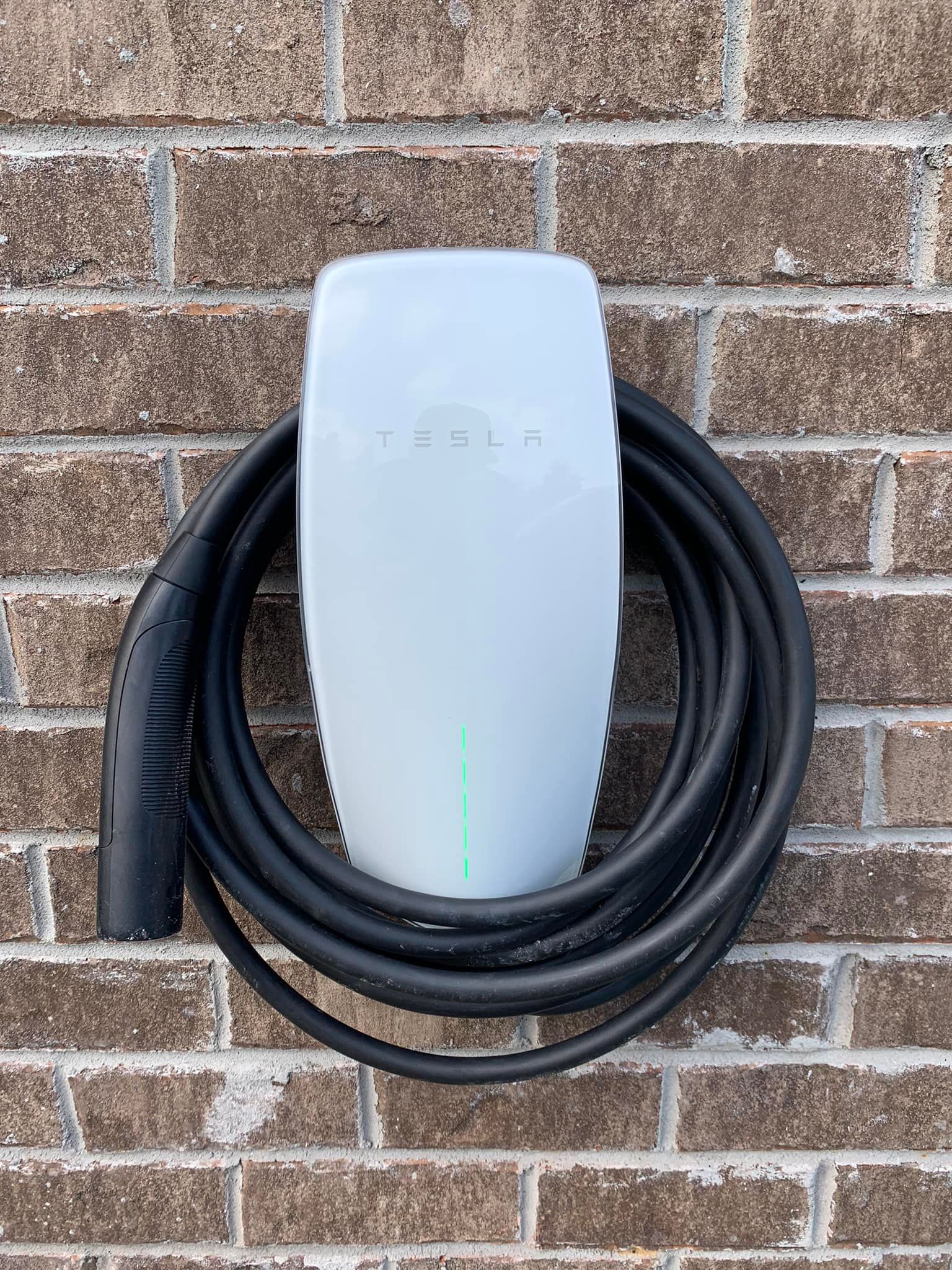 A tesla charging station is attached to a brick wall.