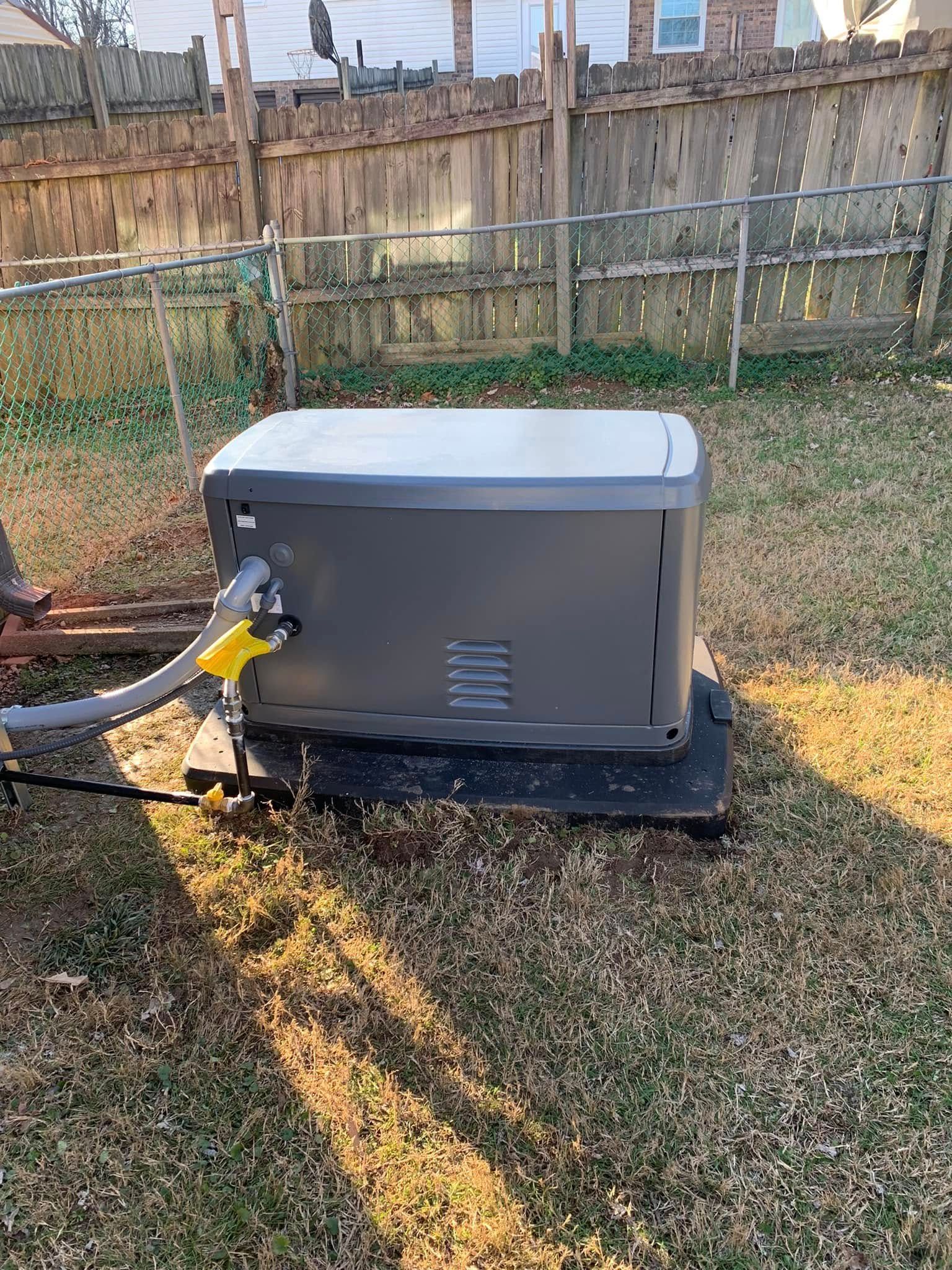 A generator is sitting in the grass in a backyard next to a fence.