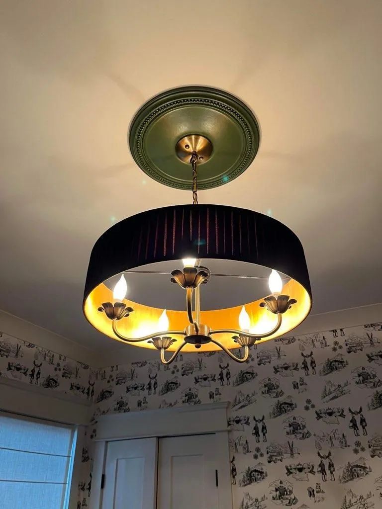 Black and gold chandelier hanging from a green ceiling plate. The room has patterned wallpaper.