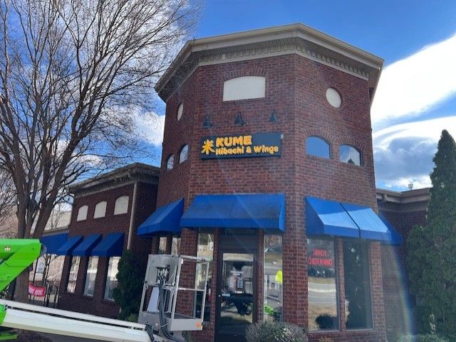 A brick building with blue awnings and a sign that says ' kume ' on it