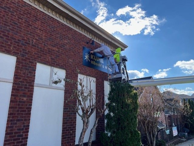 A man is painting a blue sign on the side of a brick building