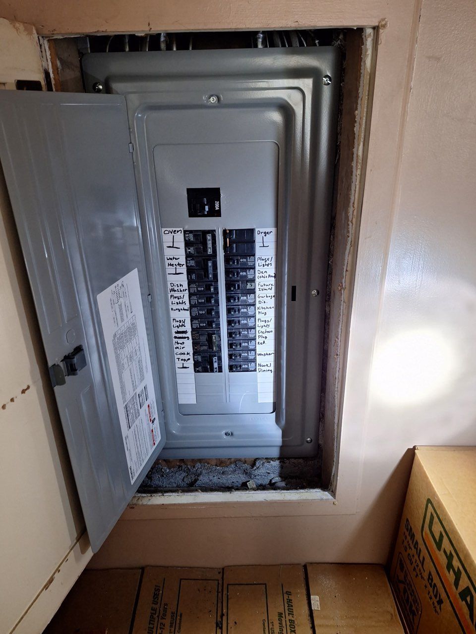 Opened gray electrical panel in a recessed wall. Paper and debris at the bottom.