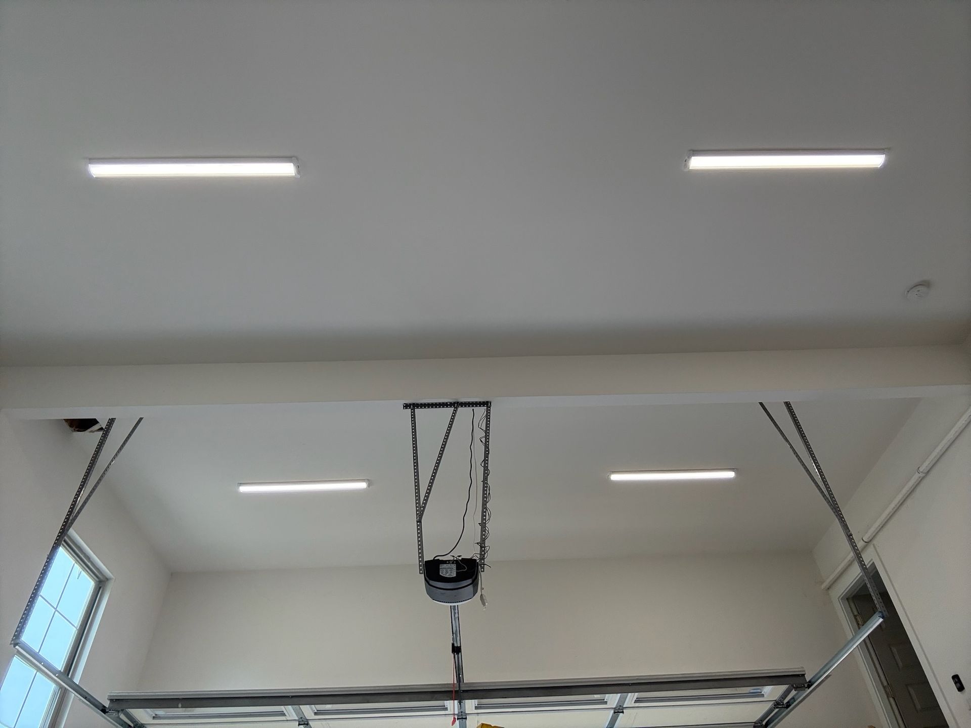 Garage ceiling with four rectangular LED lights and a garage door opener.
