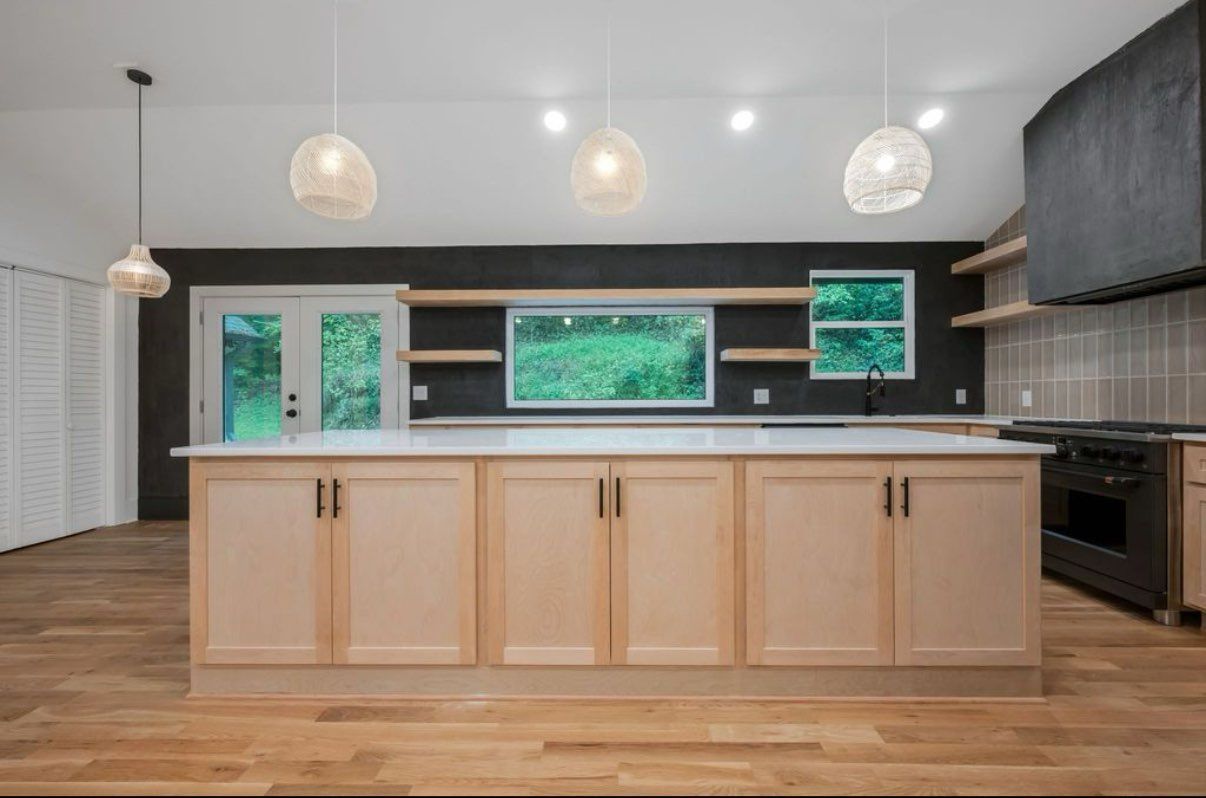 Modern kitchen with light cabinets, large island, dark backsplash, and three pendant lights.