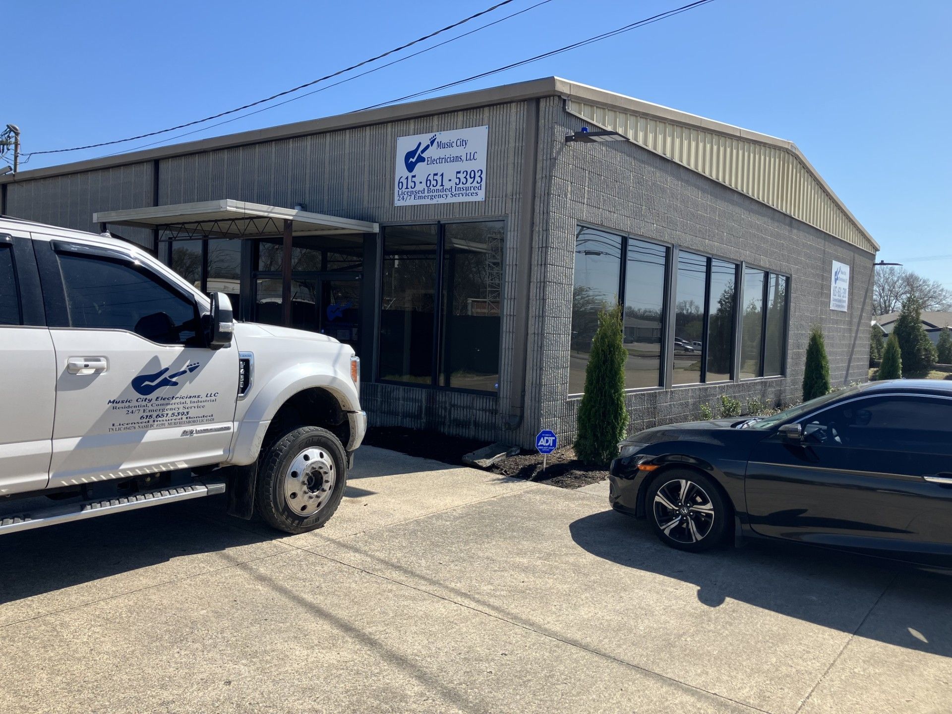 A white truck and a black car are parked in front of a building.