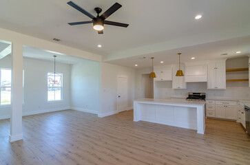 Open-concept kitchen and living area with white walls, light wood floors, and a black ceiling fan.