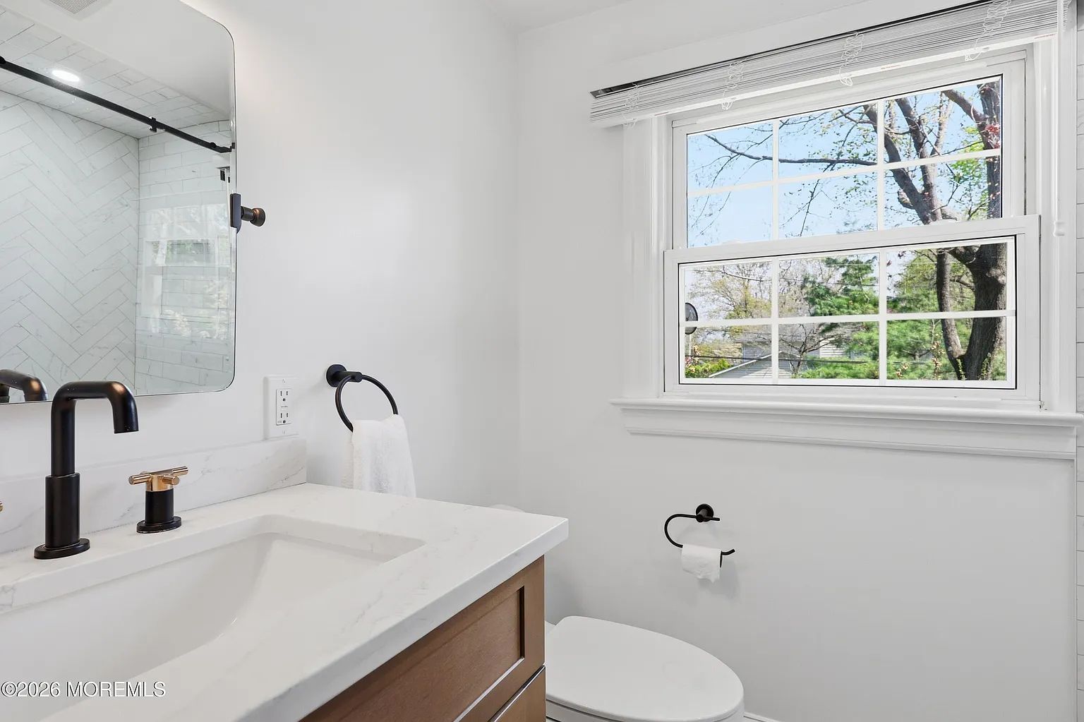 Bright modern bathroom with white walls, vanity sink, mirror, and window above the toilet