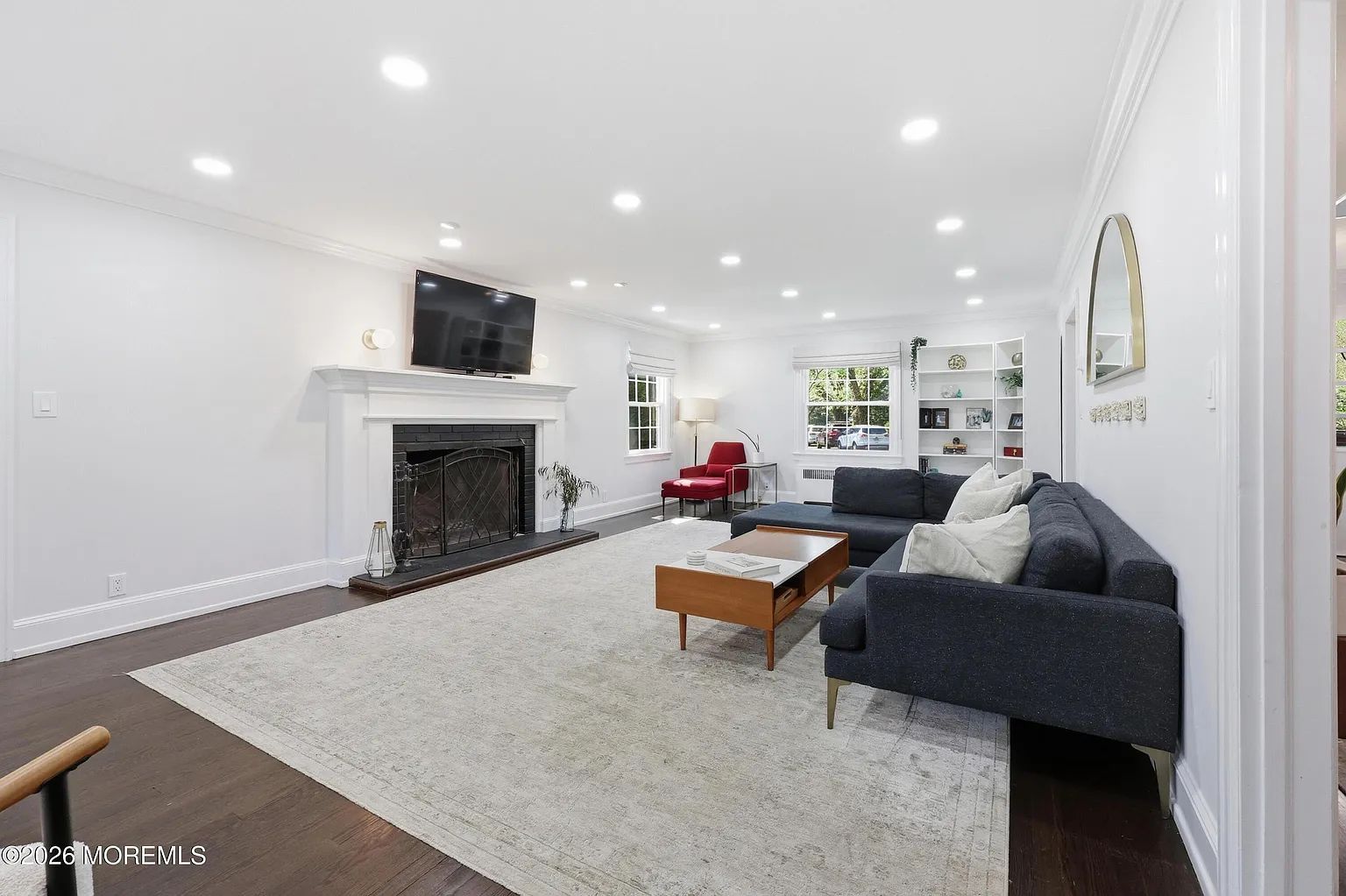 Bright living room with gray sofa, fireplace, TV, and large windows on a light carpet.