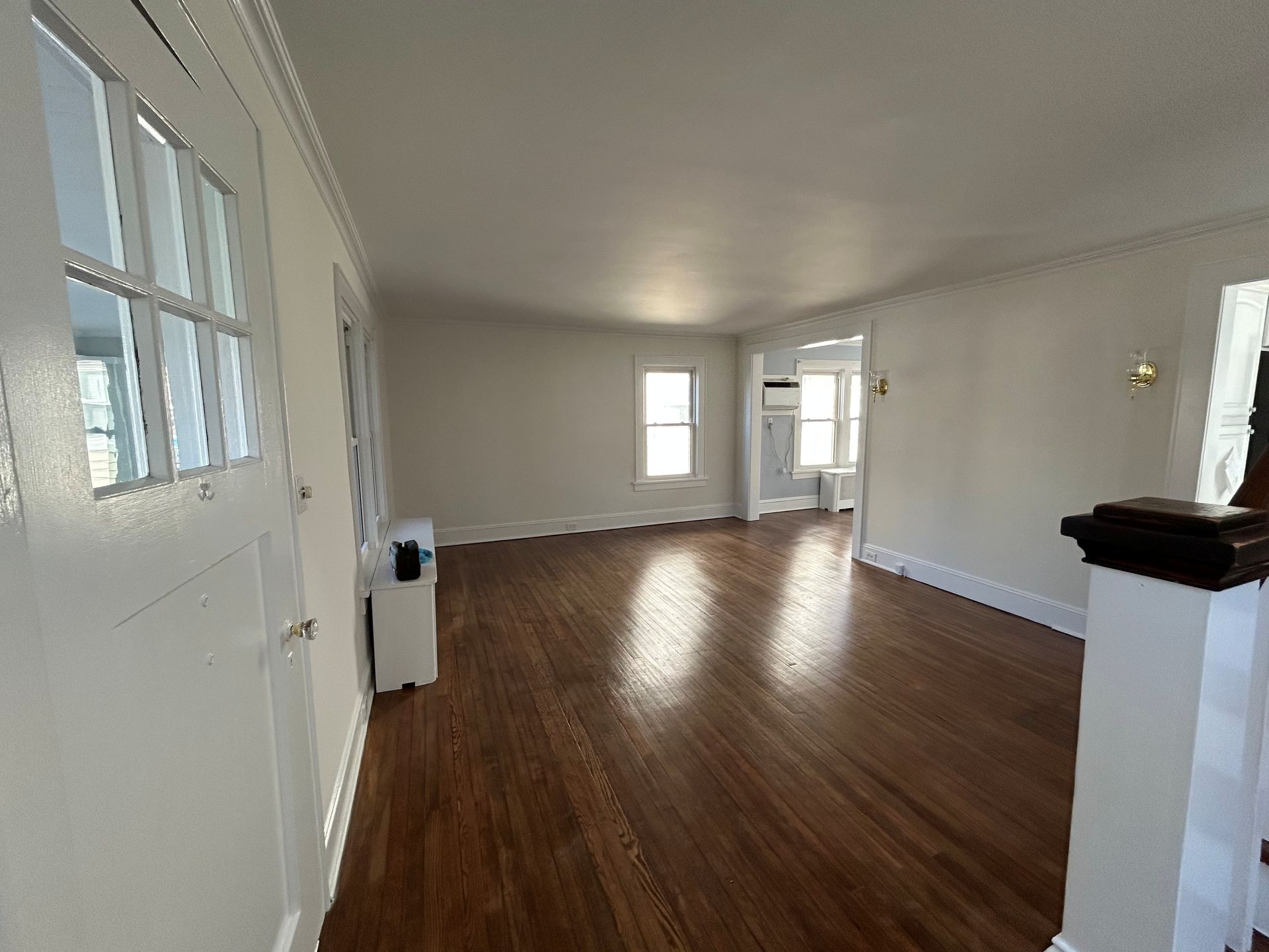 Empty living room with wood floors, white walls, and windows letting in daylight