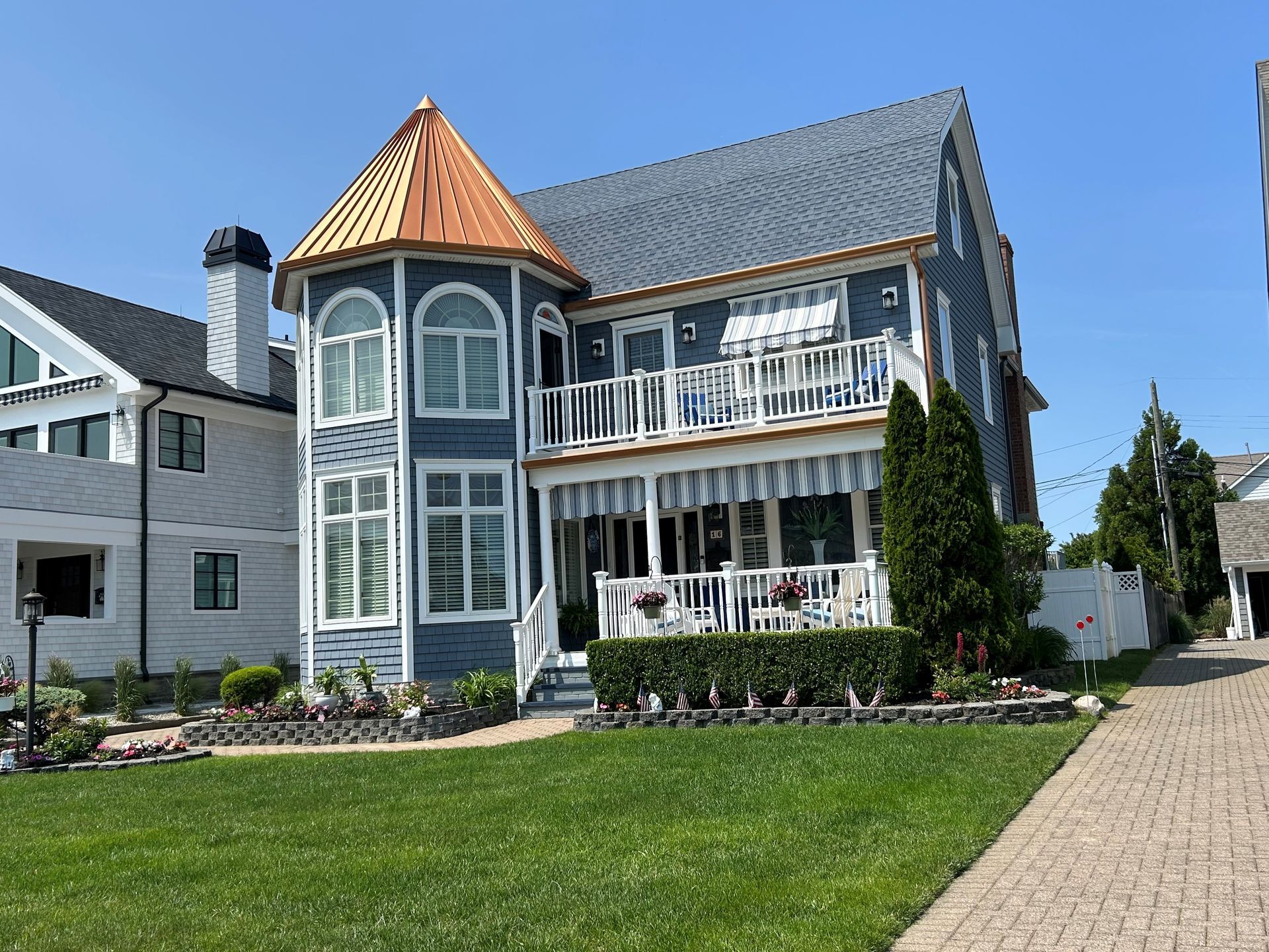 Victorian house with blue siding, copper turret, white balconies, and a green lawn by a sidewalk