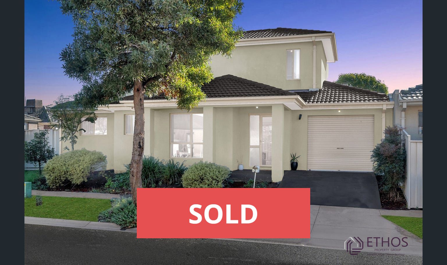 Two-story beige house with a sold sign, driveway, and small tree in front.