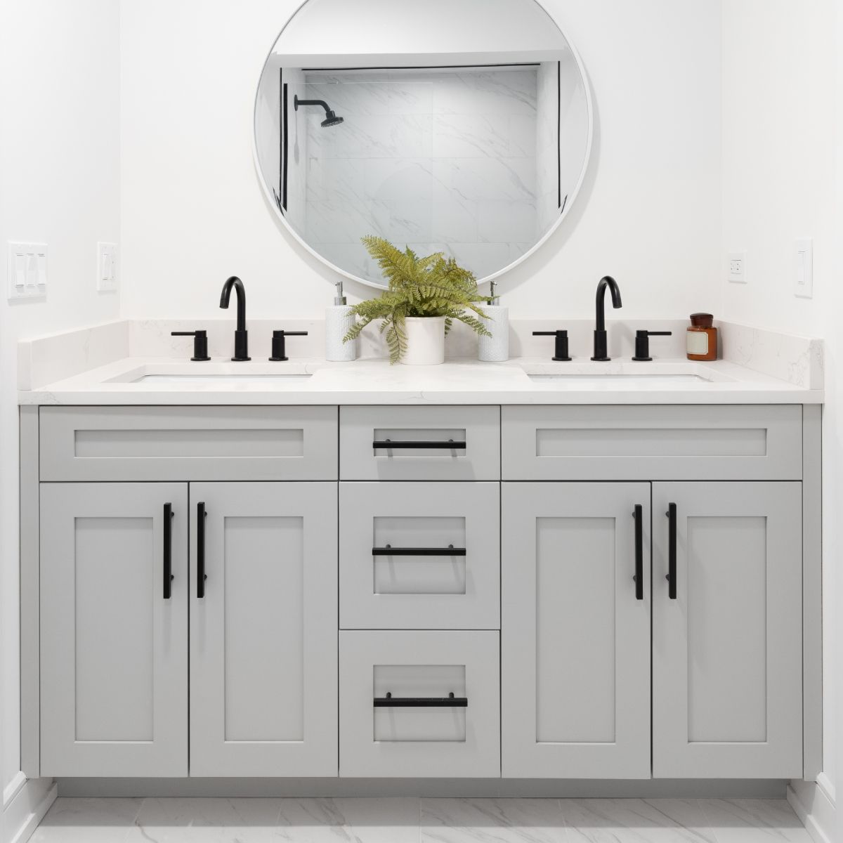 A modern bathroom with a light gray double vanity, black fixtures, and a round mirror reflecting the shower.