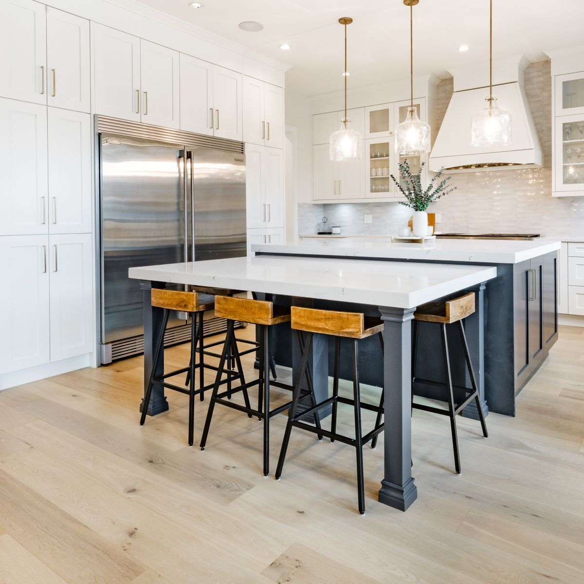 Modern kitchen with white cabinets, stainless steel refrigerator, and a dark island with wooden stools.