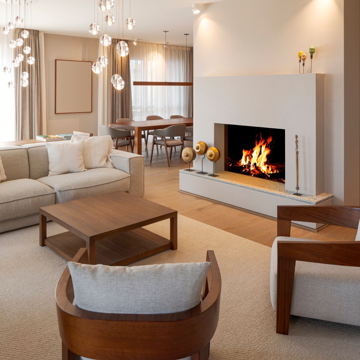 Living room with beige walls, fireplace, and wooden furniture. Fire in the fireplace, neutral-toned furnishings, and dining area in the background.