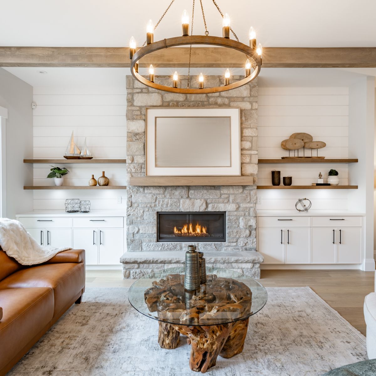 Living room with stone fireplace, built-in shelves, leather sofa, wooden coffee table, and chandelier.