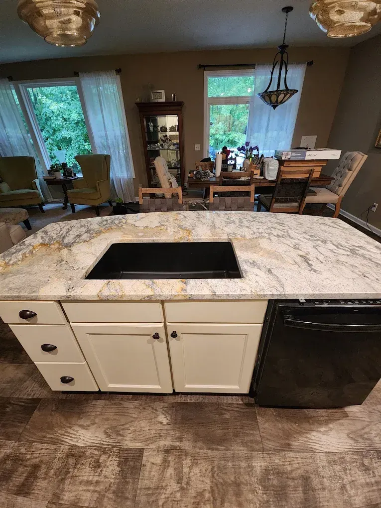 Kitchen island with a granite countertop and a built-in stovetop, white cabinets, and a black dishwasher.