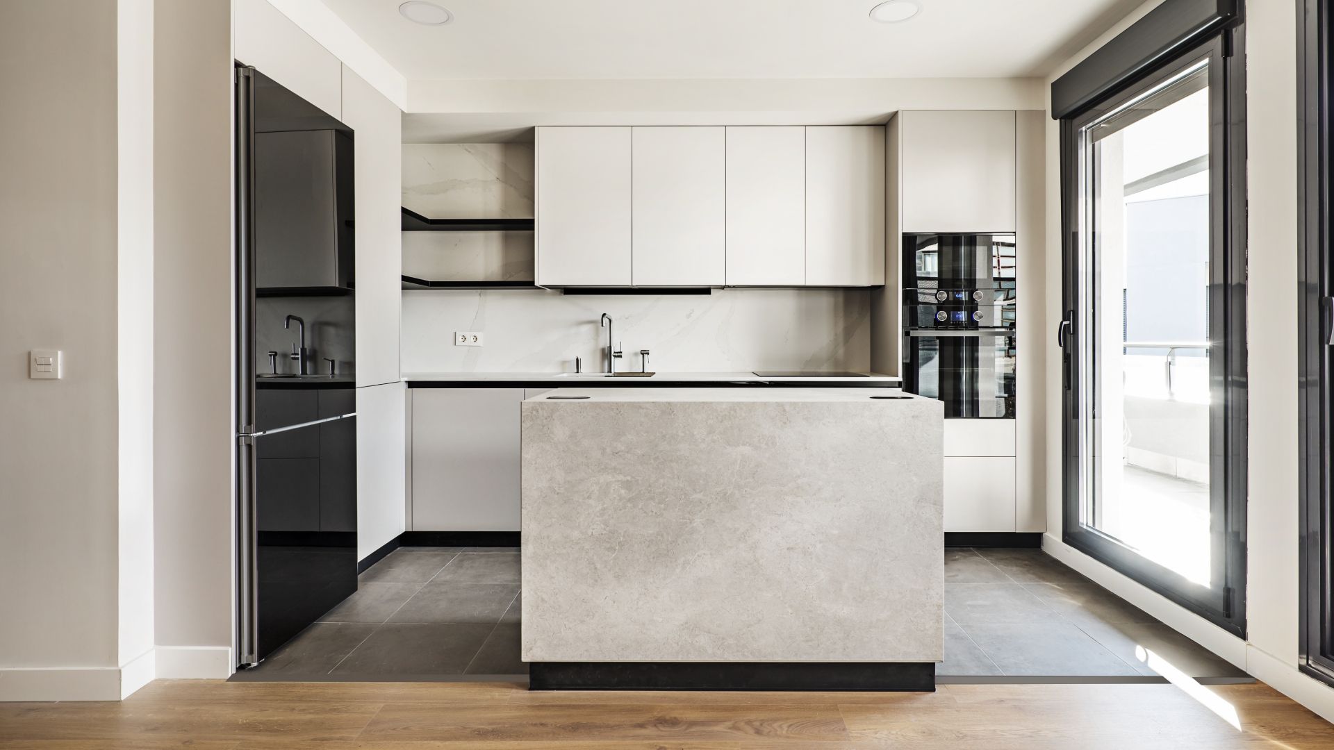 Modern white kitchen with a stone island, black accents, and large window letting in light.