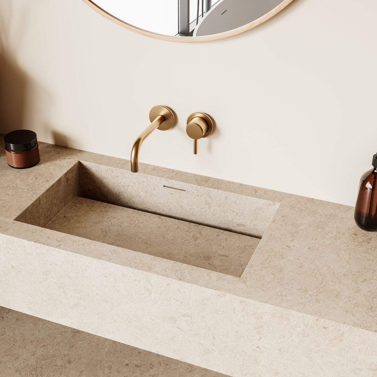 Beige rectangular bathroom sink with gold fixtures and round mirror. Soap dispensers and lotion bottle sit on the counter.