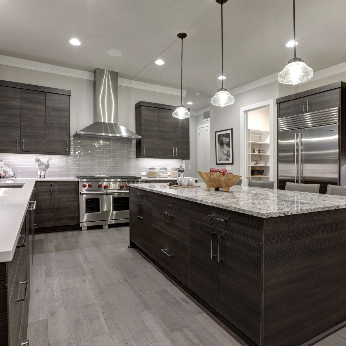 Modern kitchen with dark wood cabinets, white countertops, stainless steel appliances, and a large island.