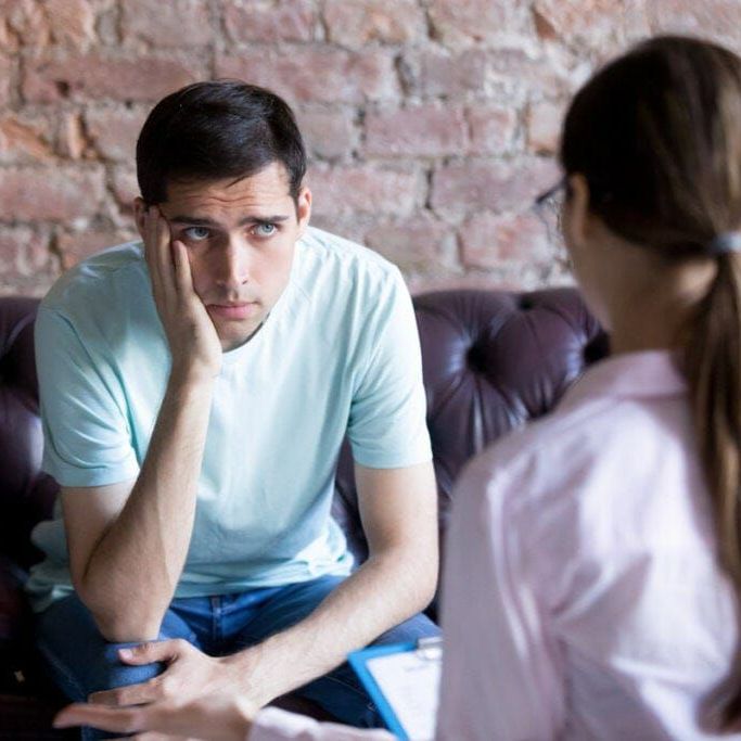 Un hombre está sentado en un sofá hablando con una mujer.
