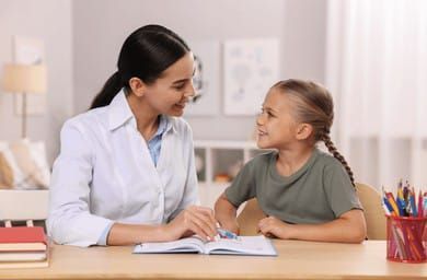 Una mujer le está enseñando a una niña a leer un libro.