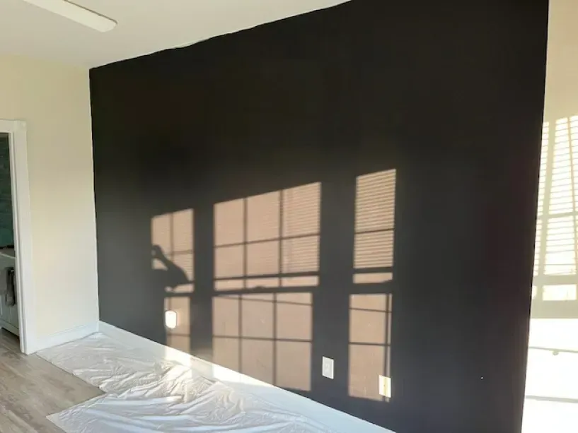 A room with a black wall and a shadow of a window on it.